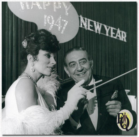 Joan Collins (Lady Daisy Frawley) zwaait met een sigarettenhouder in een poging om Guy Lombardo's dirigeer techniek onder de knie te krijgen.